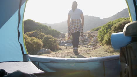 hiking on mountain trail, woman walking away from tent in morning light