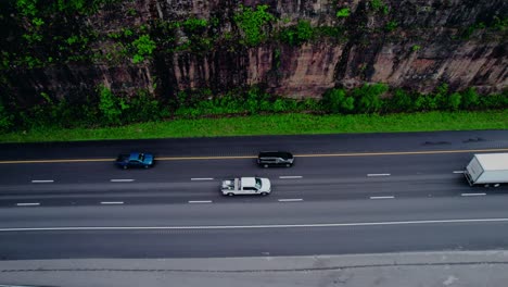 top-down aerial of a stepdeck semi truck hauling construction equipment along a cliffside highway.