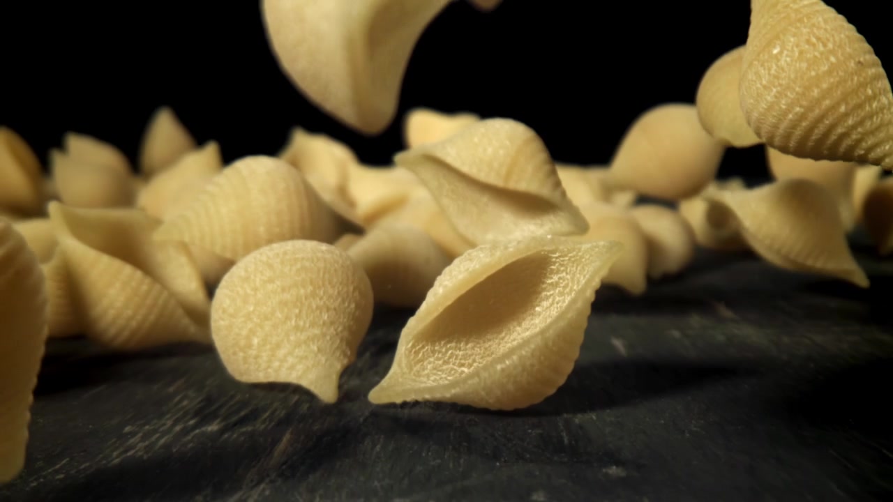 Conchiglie di pasta che cadono su una superficie scura al rallentatore