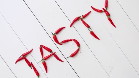 a word tasty formed with small red chilli peppers  placed on white wooden table