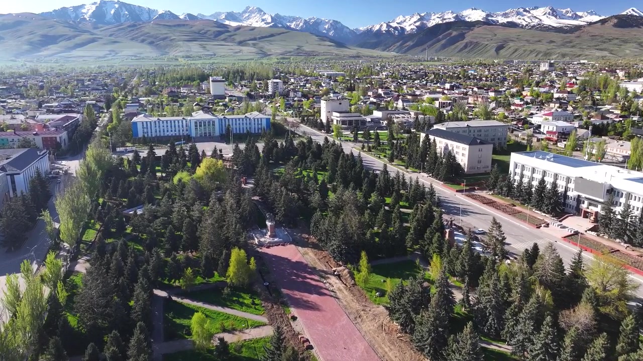 Stadspark met standbeeld en universiteitsgebouw. Stadsgezicht van Karakol, Kirgizië, met bergen. Luchtfoto