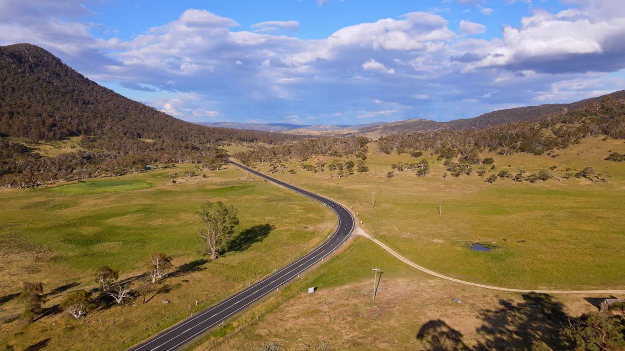 vista de avión no tripulado de un automóvil conduciendo en una carretera de campo con tierras de cultivo rurales cubiertas de hierba en un día soleado, crackenback, nueva gales del sur, australia