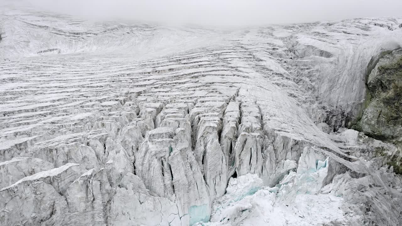 Aerial flyover over the edge of the Moiry glacier near Grimentz in Valais, Switzerland with a spinning view of the icy crevasses, valley and lake on a cloudy summer afternoon