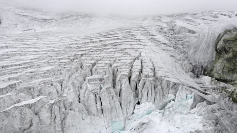 aerial flyover over the edge of the moiry glacier near grimentz in valais, switzerland with a spinning view of the icy crevasses, valley and lake on a cloudy summer afternoon