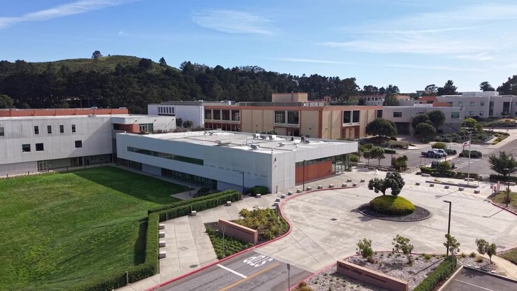 Prospettiva aerea pomeridiana che mostra l'architettura moderna dello Skyline College a San Bruno, California, in una giornata di sole con prati verdi e colline circostanti. Ripresa con zoom filmata in 4K.