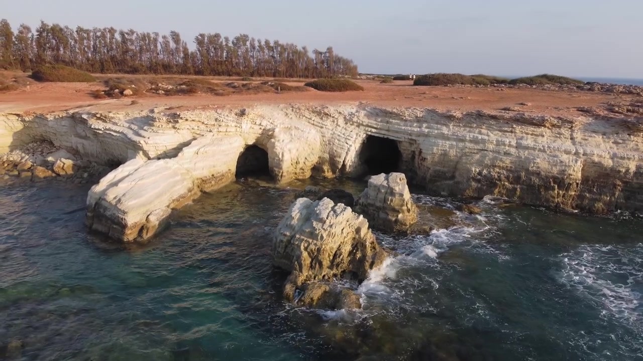 Una costa rocciosa presenta grotte marine naturali scavate dalle onde dell'oceano sotto un cielo sereno.