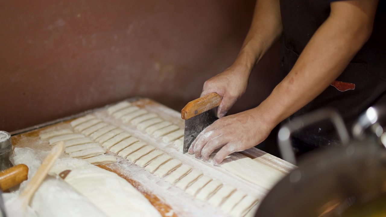 Close-up of baker's hands using a metal scraper to cut dough on floured surface.