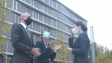 colegas de trabalho com máscaras faciais se encontrando do lado de fora, cumprimentando-se com cotoveladas e conversando