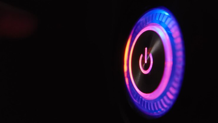 A person's finger presses the computer start button. Illuminating button to turn on the computer on the system unit. 4k macro loop video.