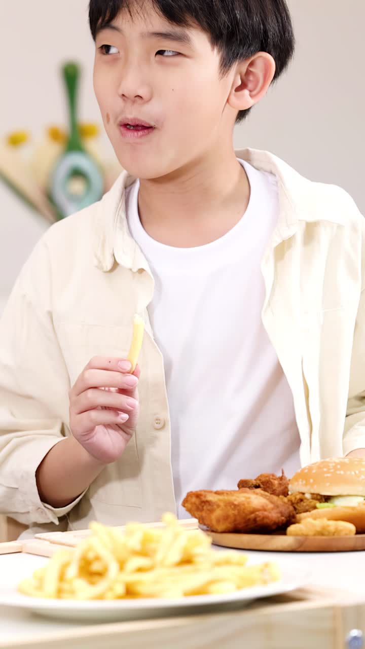 明るい教室のランチテーブルでフライドポテトとフライドチキンを楽しむ笑顔の男子生徒、ミディアムクローズアップ。