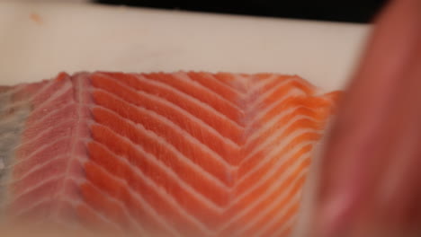 experienced chef trimming the meat of a fresh salmon fillet using a knife for sushi dish