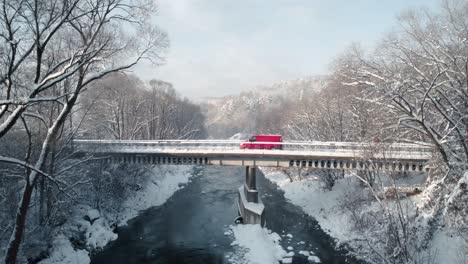 Toma-Aérea-De-Una-Furgoneta-Roja-Cruzando-El-Puente-Nevado-En-La-Mañana-De-Invierno