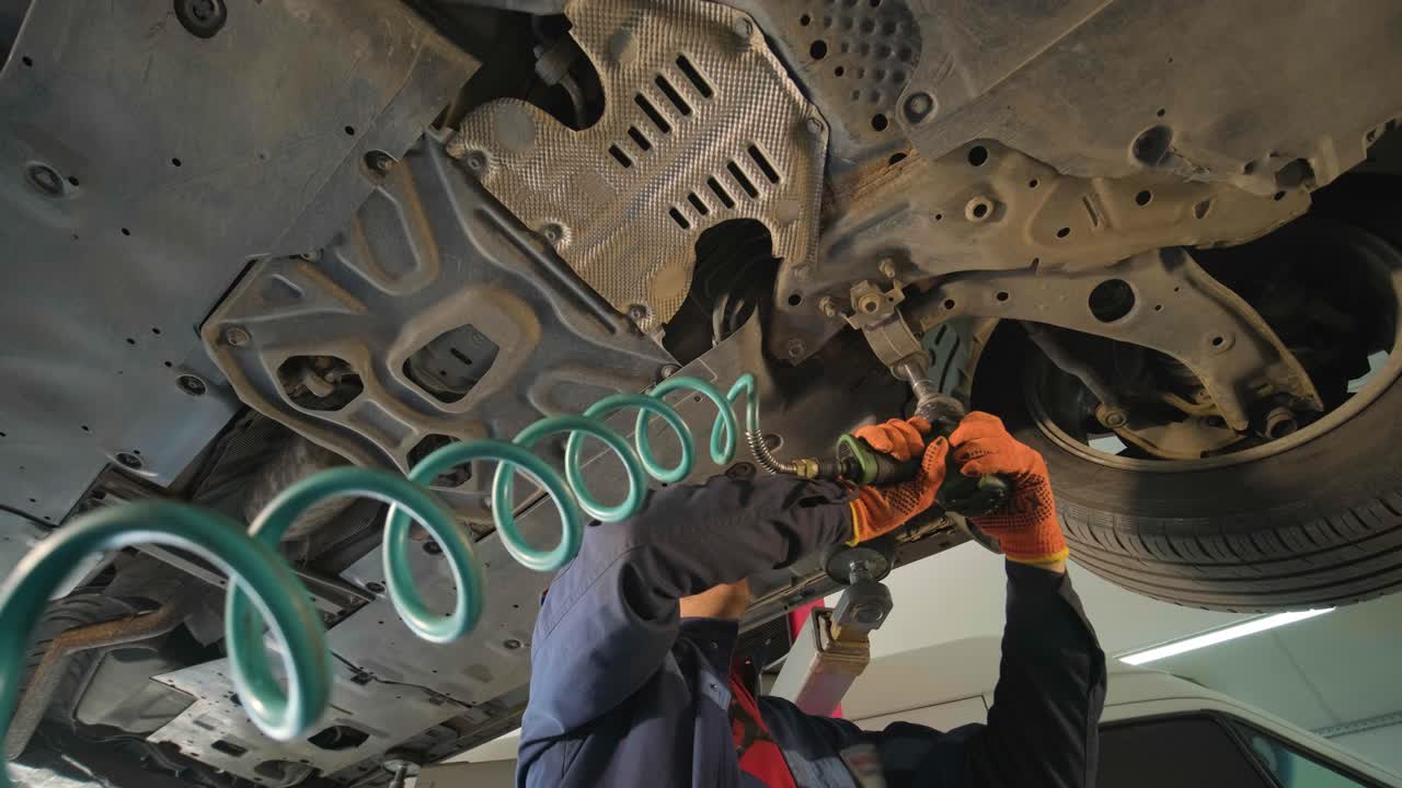 joven mecánico profesional que trabaja bajo el coche moderno levantado en el servicio de reparación de automóviles. servicio de automóviles, mantenimiento de reparación.