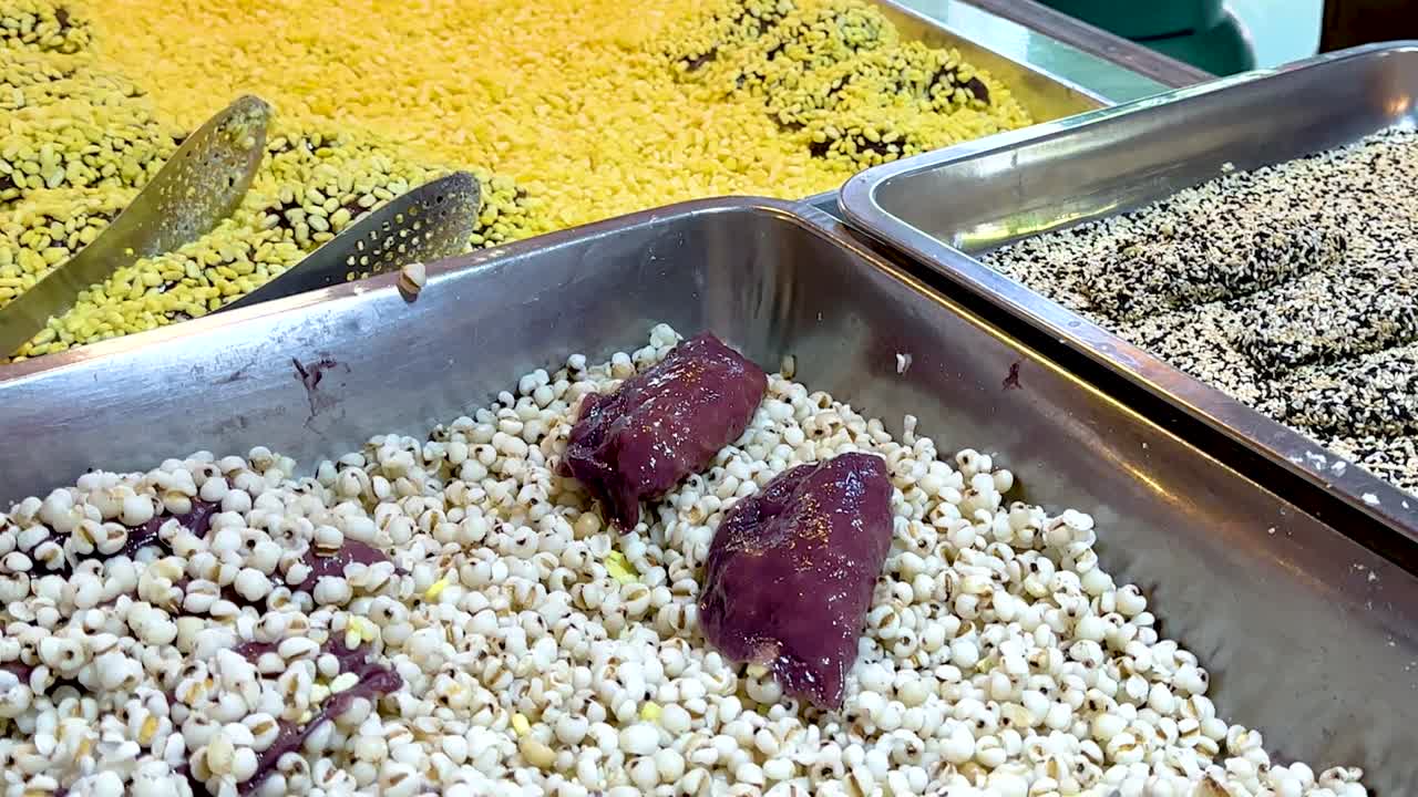 Close-up view of assorted grains and seeds in metal trays at a market stall.