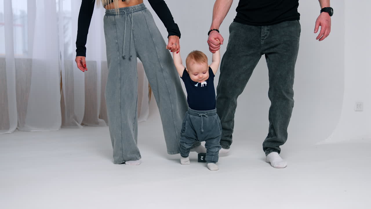 Unrecognized man and woman hold a little baby by the hands. Parents teach their infant son to walk.