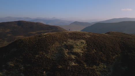 hiker on distant hilltop with slow rise up and distant misty mountain range at english lake district uk