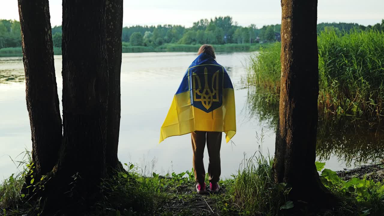 Woman draped in national flag stands quietly by riverbank at golden sunset
