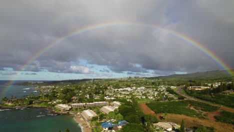 perfect vibrant rainbow over tropical coastline and hotels with grey clouds, maui