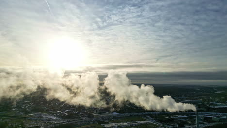 industrial smog from a chimney with cityscape background, sunny day - aerial view