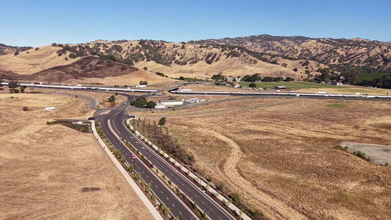 Veduta aerea dello svincolo autostradale della Interstate 80 vicino al Lagoon Valley Park a Vacaville, California, che mostra il traffico che scorre attraverso le colline aride e dorate in una giornata di sole.