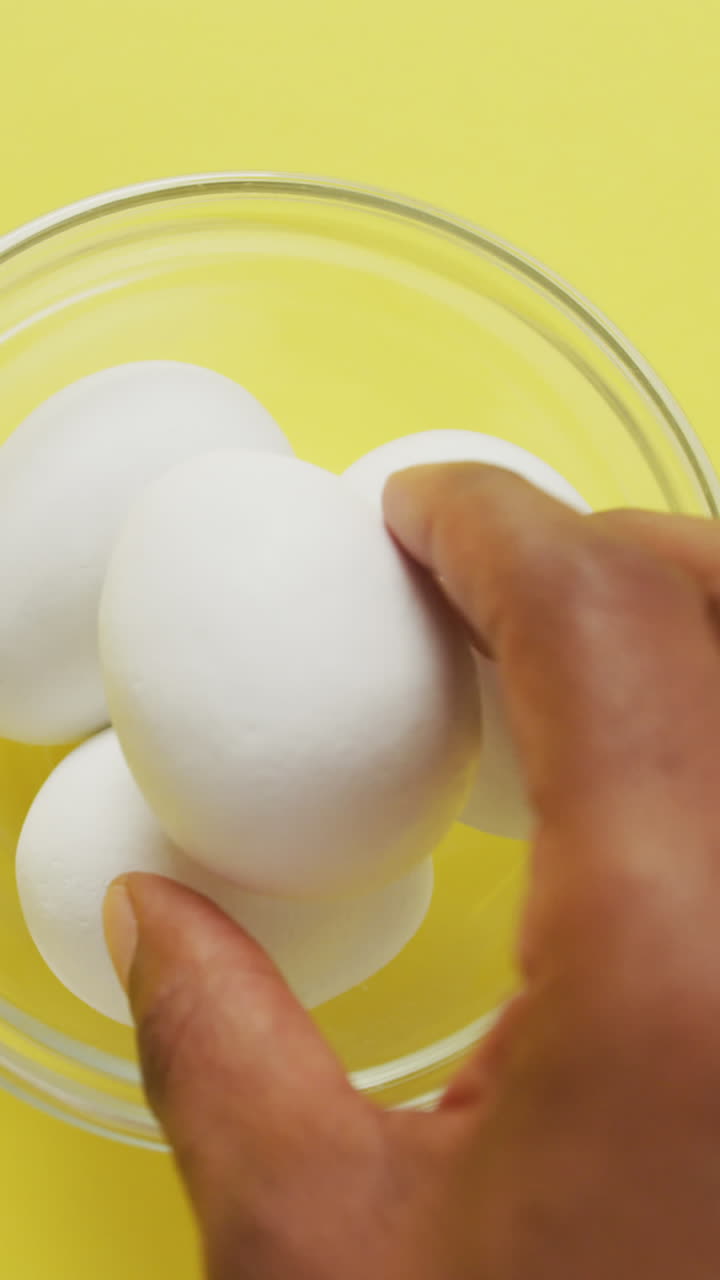 Video of overhead view of glass bowl with eggs on yellow background