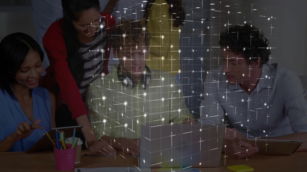 Four colleagues gathering around table, discussing tech design while 3D cube forming above laptop