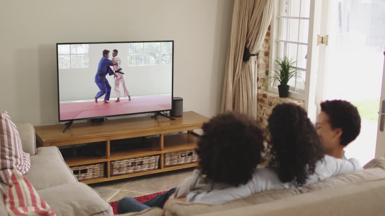 Famiglia felice seduta insieme a casa che guarda un incontro di judo in TV.