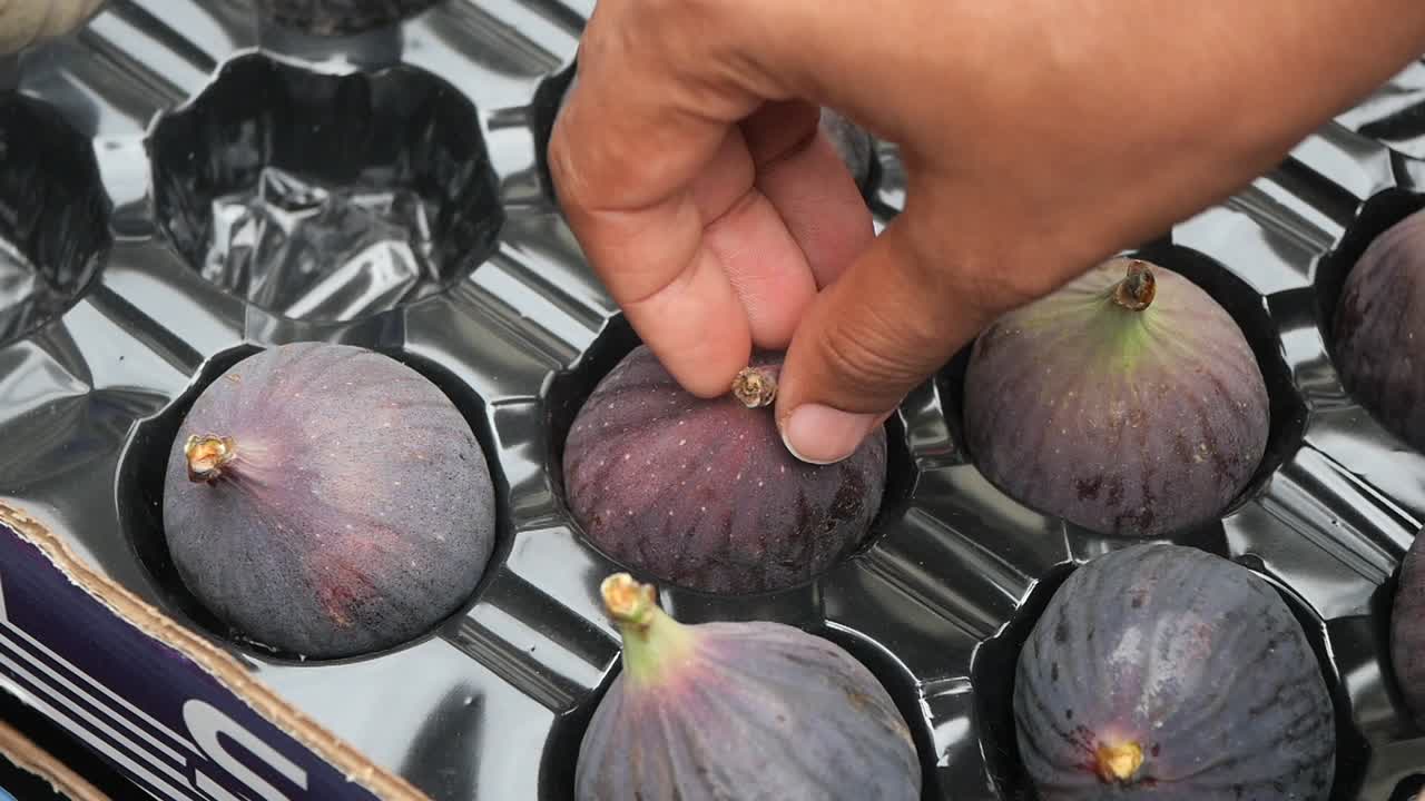 A Hand Picking Ripe Figs From a Box at a Farmers Market