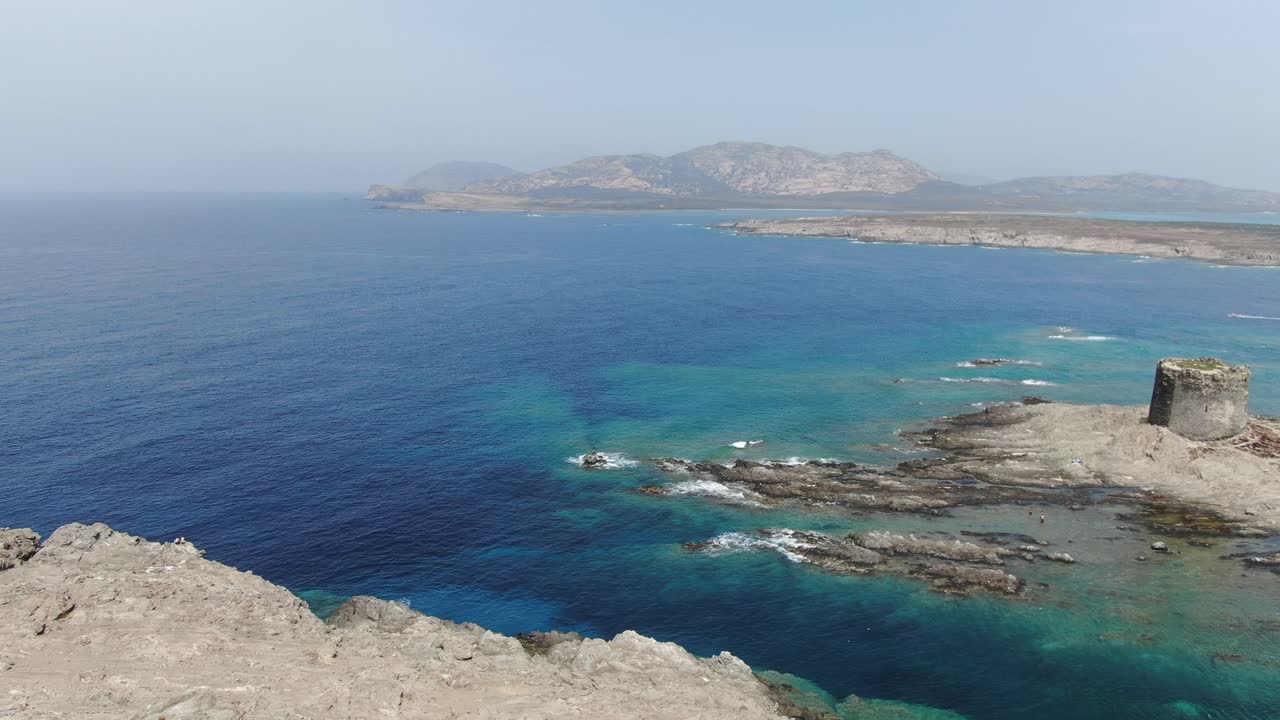 This video follows a 360 degree view of rocky cliffs near a lone castle that resides close to a coastline along a city