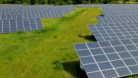 Solarkraftwerkspanels-Mitten-Auf-Der-Grünen-Wiese,-Luftüberführung-Mit-Niedrigem-Winkel-Polen