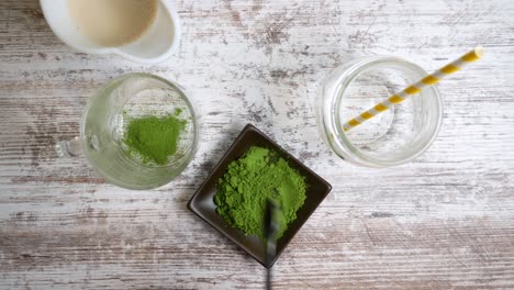 spooning green tea matcha powder into a glass cup then pouring hot water into the glass