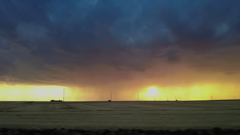 Dark-storm-clouds-over-golden-yellow-sunset-countryside,-driving-POV