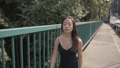 Plano-Medio-De-Una-Hermosa-Mujer-Asiática-Vestida-De-Negro-Caminando-Cerca-De-Una-Barandilla-Verde,-En-Cámara-Lenta