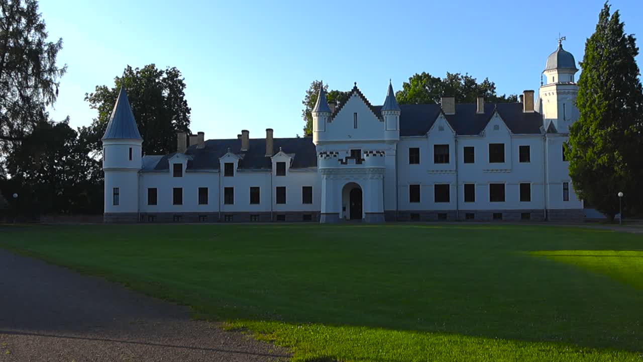Majestic white colored large castle in Alatskivi Estonia during a summer or spring sunny day. Castle is like a dream with high turret towers and sharp pointy ends, blue sky and horizon in the back