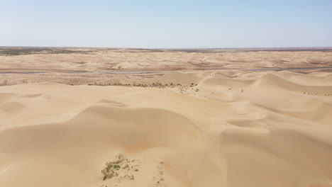 panning drone shot of sand dunes lining a car road in the gobi desert