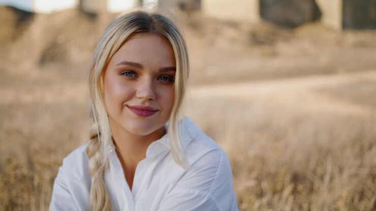 une femme ensoleillée assise sur un pré en gros plan. une femme rêvant qui regarde la caméra sur un champ d'été.