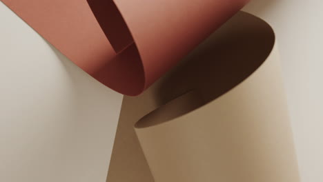 close up of two shades of brown rolled papers on white background with copy space in slow motion