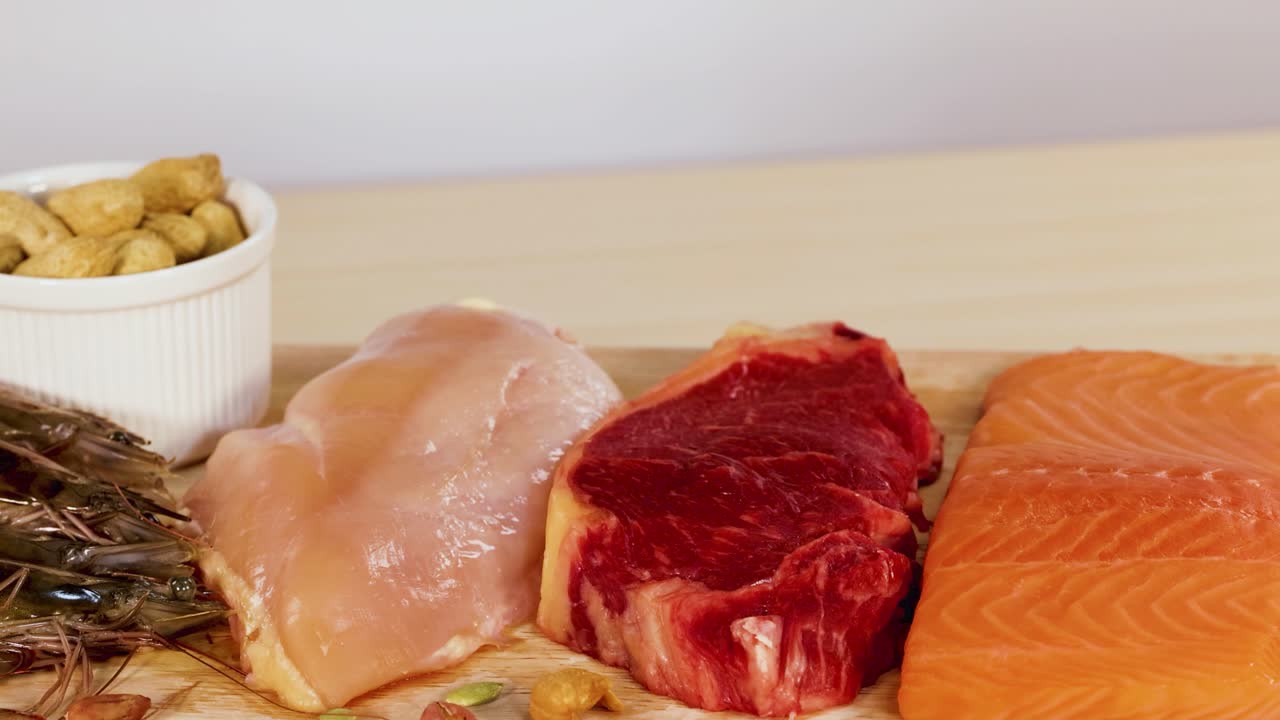 A variety of protein-rich foods including meats, nuts, and fish are artfully arranged on a wooden surface