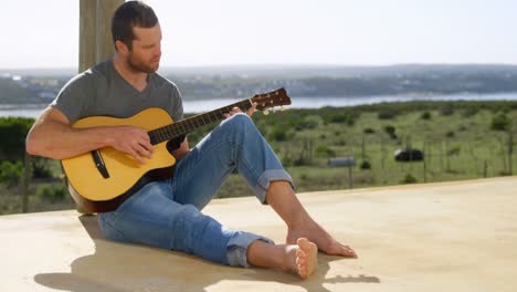 Vorderansicht-Eines-Kaukasischen-Mannes,-Der-Auf-Der-Veranda-Des-Strandhauses-Gitarre-Spielt,-4k