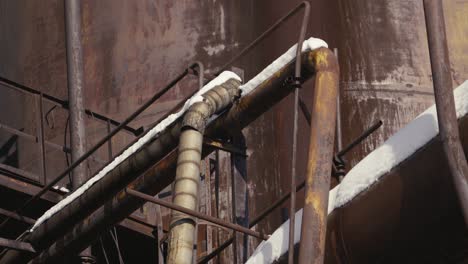 close-up of rusty industrial pipes and structures, with snow accumulated on top of them