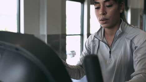 Latina-millennial-using-her-phone-while-on-an-exercise-bike-at-the-gym-stabilized-shot-in-4K-UHD