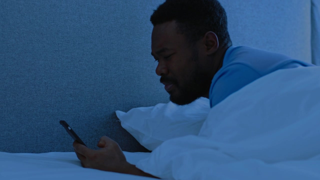 Giovane uomo che si sveglia e controlla lo smartphone a letto di notte