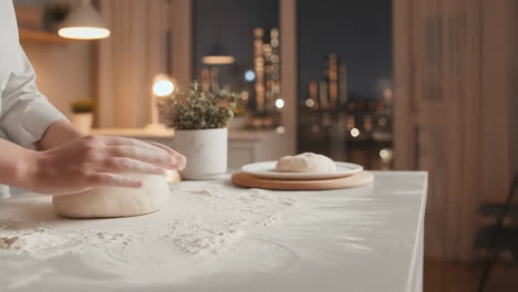 Hands kneading dough on a floured surface in a kitchen at night