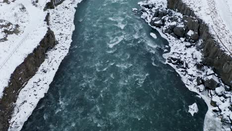 cold and icy skjalfandafljot river flowing between snowy banks and rocks in winter - north iceland,europe - aerial tilt up shot