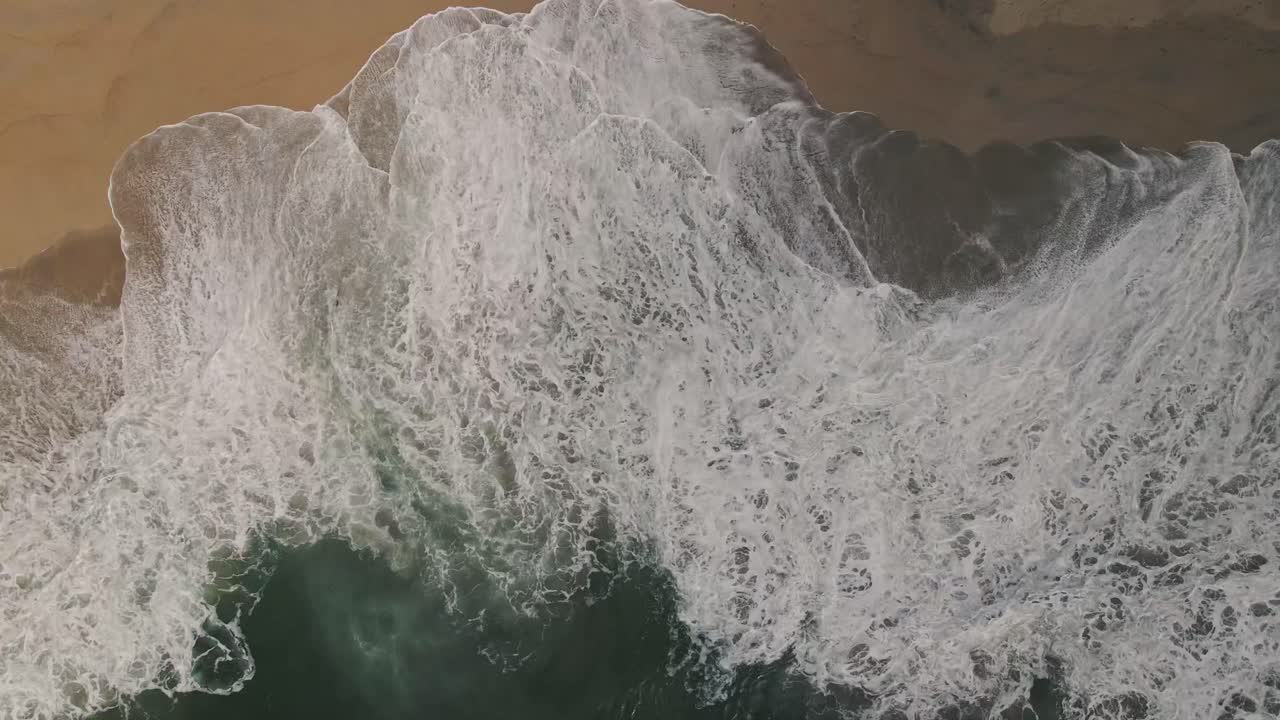 A fast moving, top-down aerial drone time-lapse of turquoise Pacific ocean saltwater crashing on a scenic empty beach north of Santa Cruz California off of the historic Highway 1