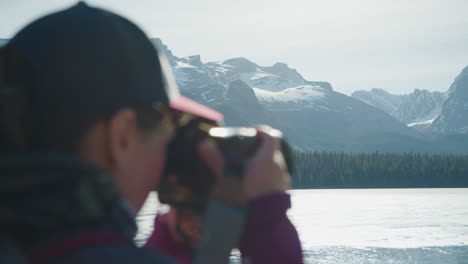 Woman-Takes-Pictures-of-Ice-Covered-Maligne-Lake,-Background-in-Focus