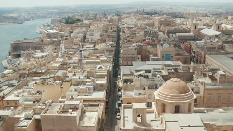 Above-the-Rooftops-of-Valletta,-Malta-Capital-City-tilt-down-to-Aerial-Birds-Eye-View-of-Beige-Sand-Colored-Houses-and-Ocean-View