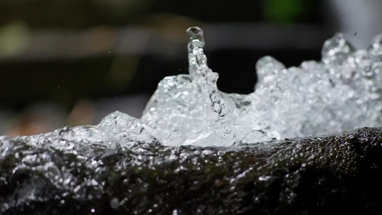 Clear fresh water bubbles up and splashes vigorously over the edge of a wet dark stone.