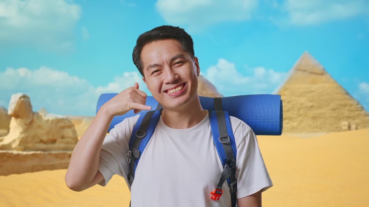 Close Up Of Asian Male Hiker With Mountaineering Backpack Smiling And Showing Call Me Gesture While Traveling In Pyramid Of Giza