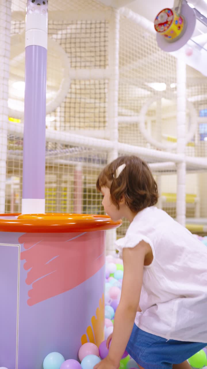 Little girl having fun in a colorful ball pit, playfully learning about physics by throwing balls into a suction machine - Slow motion vertical